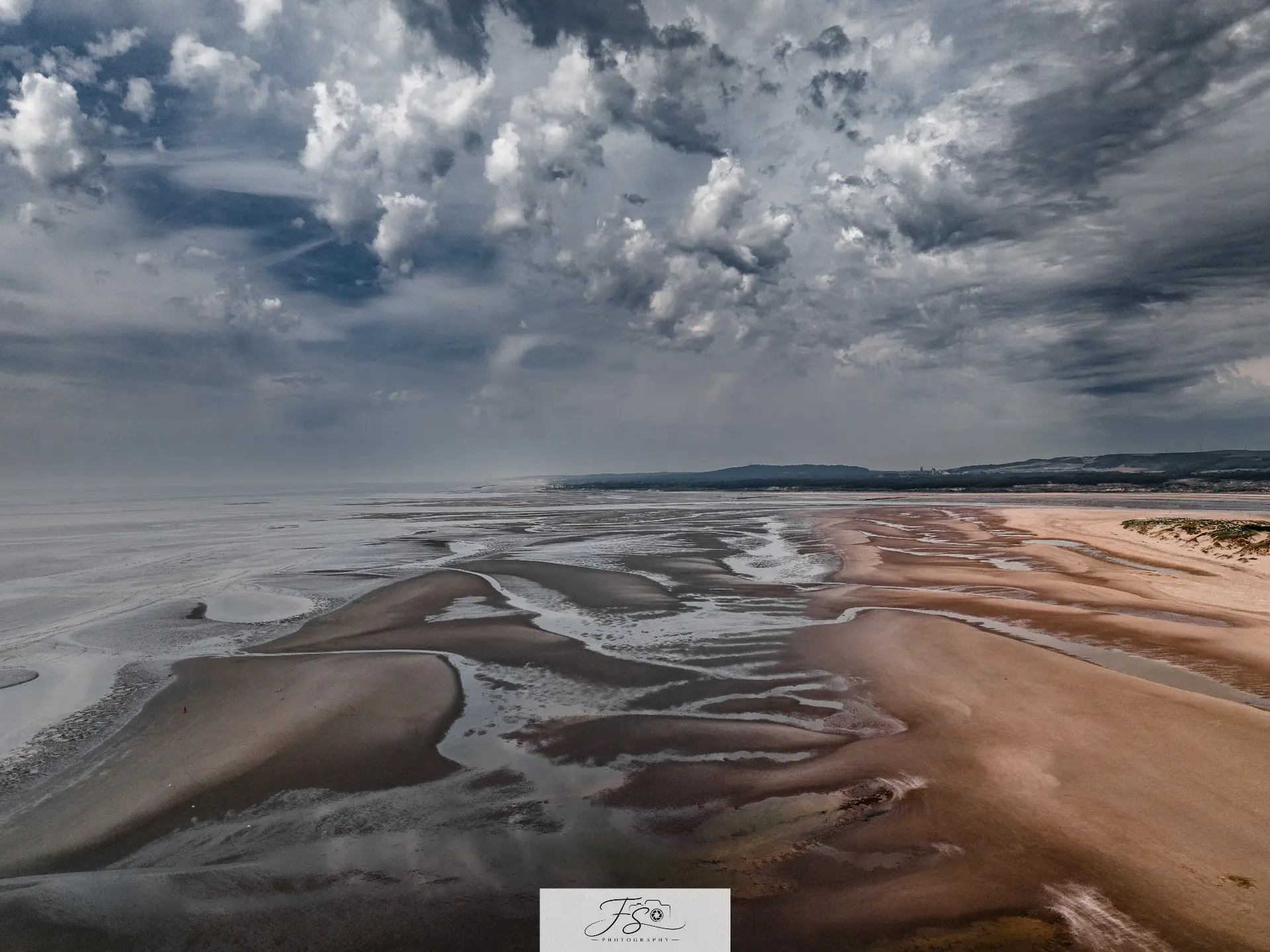 Marée graphique — vaste plage à marée basse sous un ciel de nuages sculptés