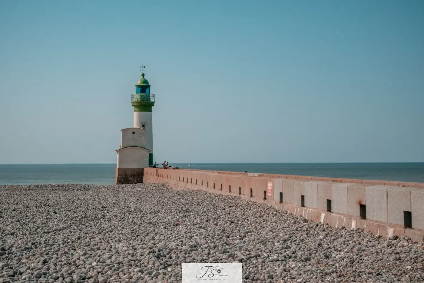 Le phare de la jetée — phare blanc et vert prolongeant une jetée de galets face à la mer