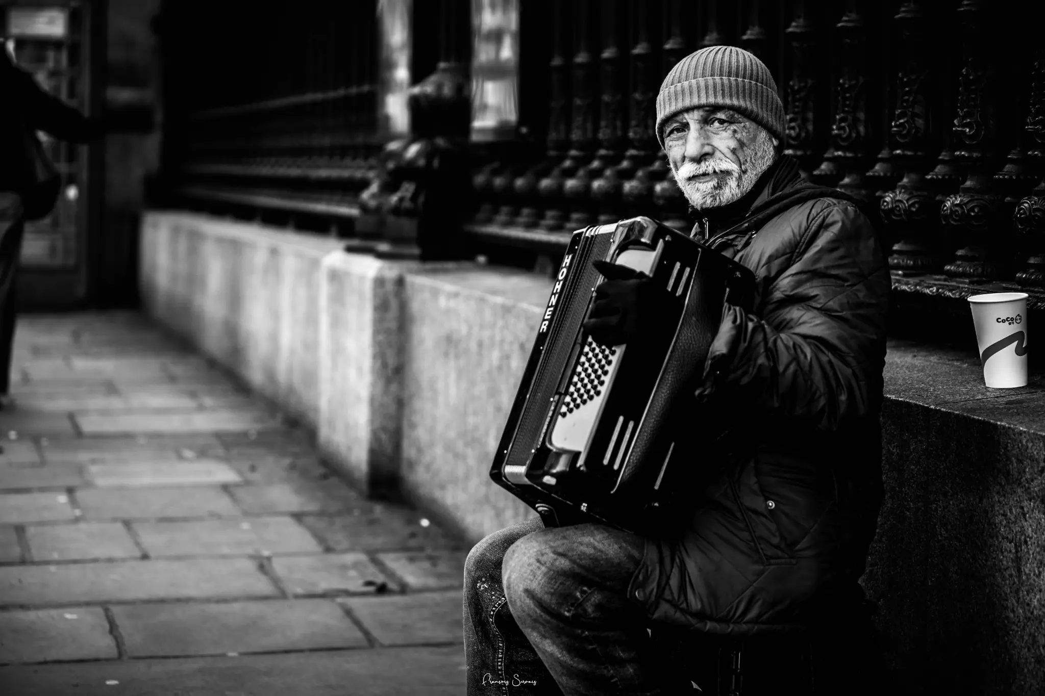 Accordéoniste de rue assis près d’un escalier dans une scène en noir et blanc
