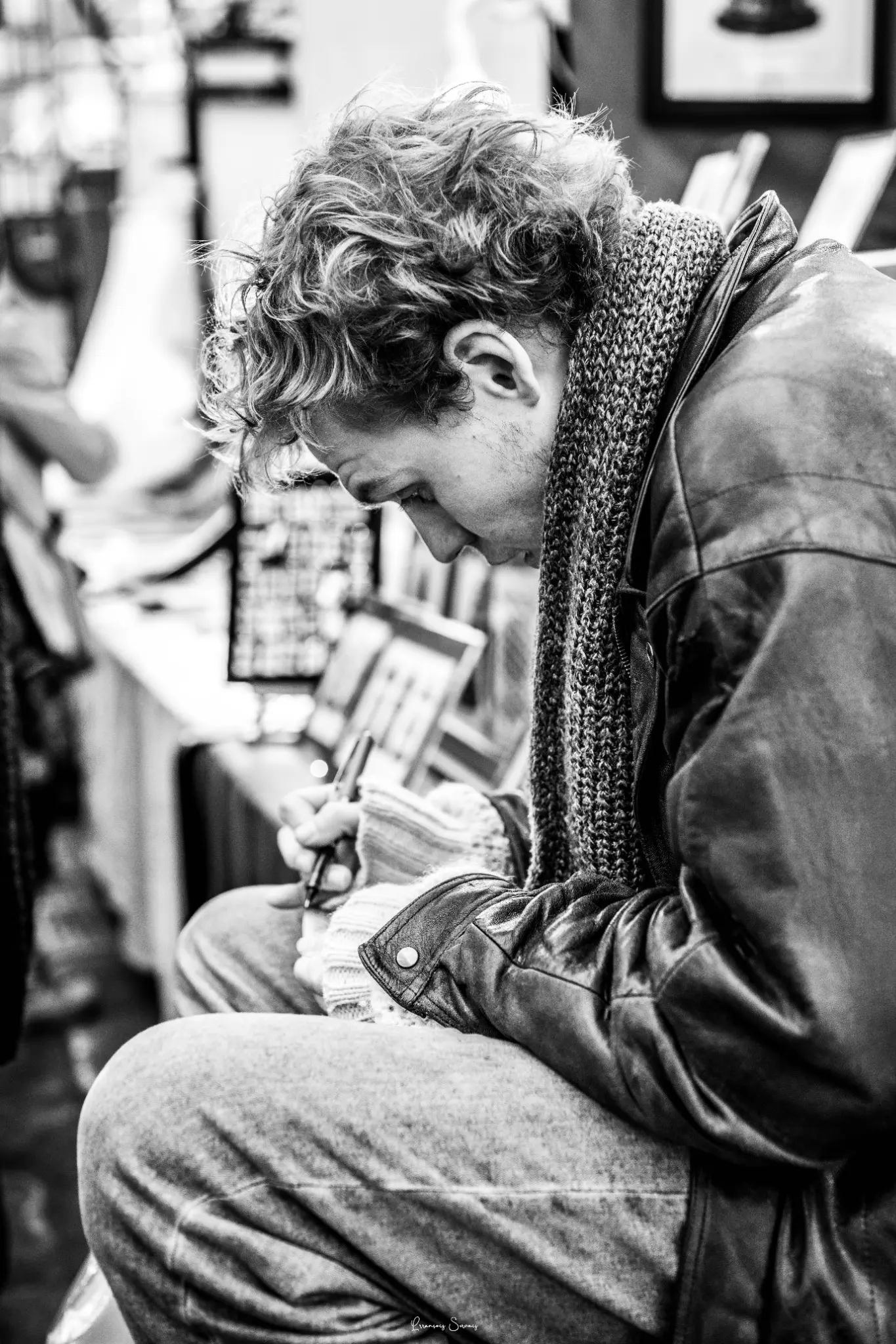 Jeune homme assis, absorbé par son carnet, dans un portrait vertical en noir et blanc