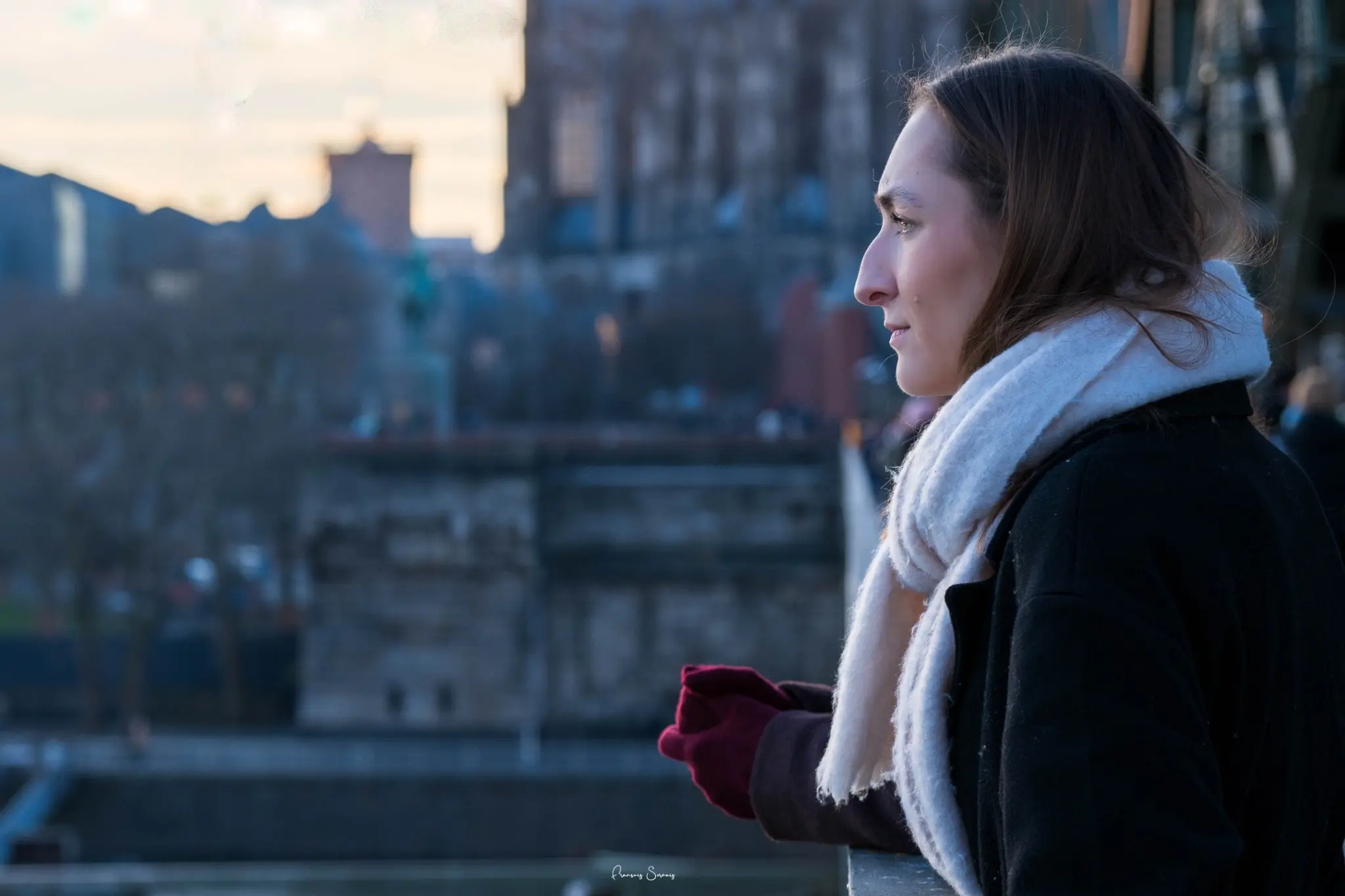 Jeune femme de profil, enveloppée dans une écharpe blanche, regardant la ville au bord de l’eau