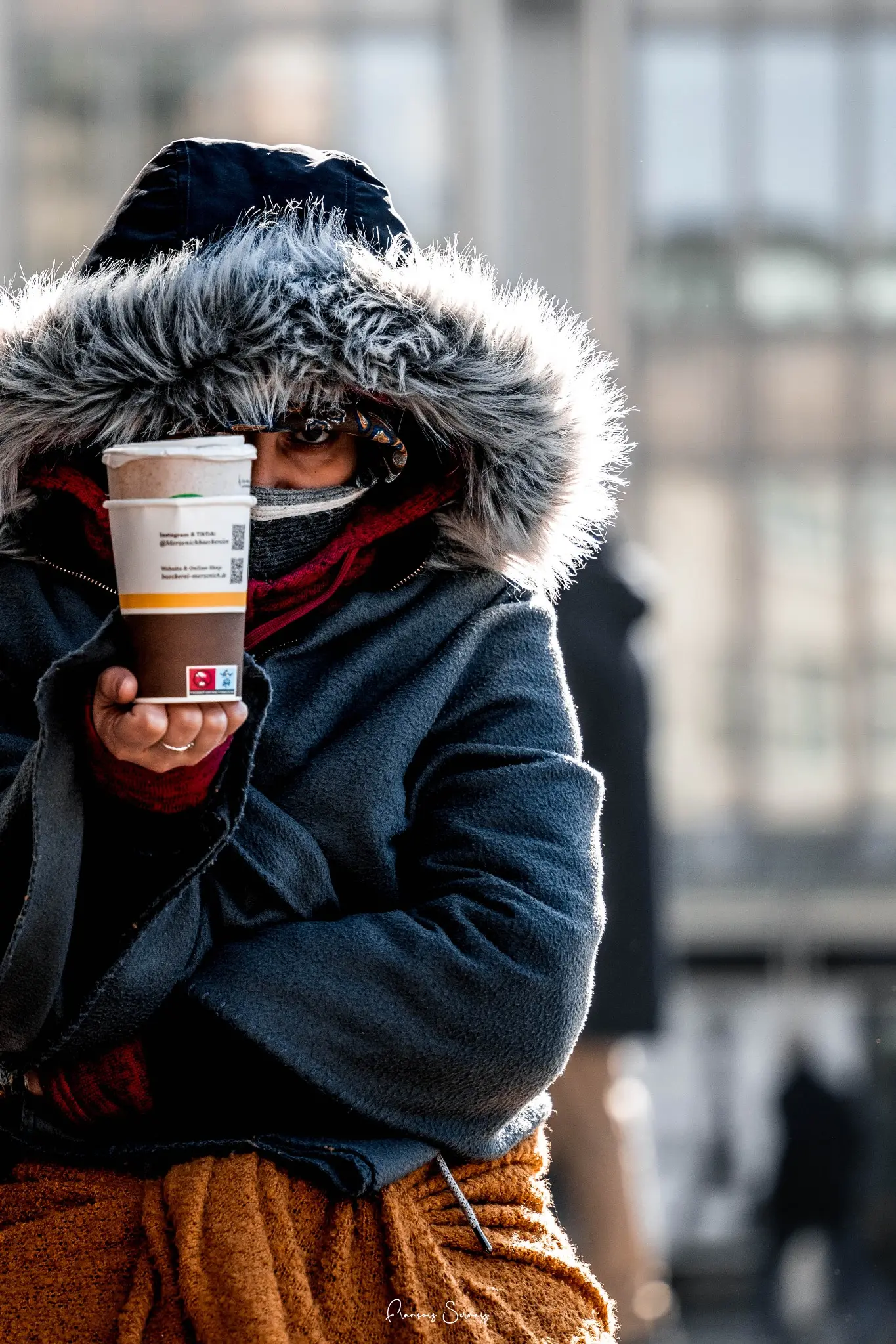 Portrait rapproché d’une femme emmitouflée dans une capuche, une tasse chaude à la main