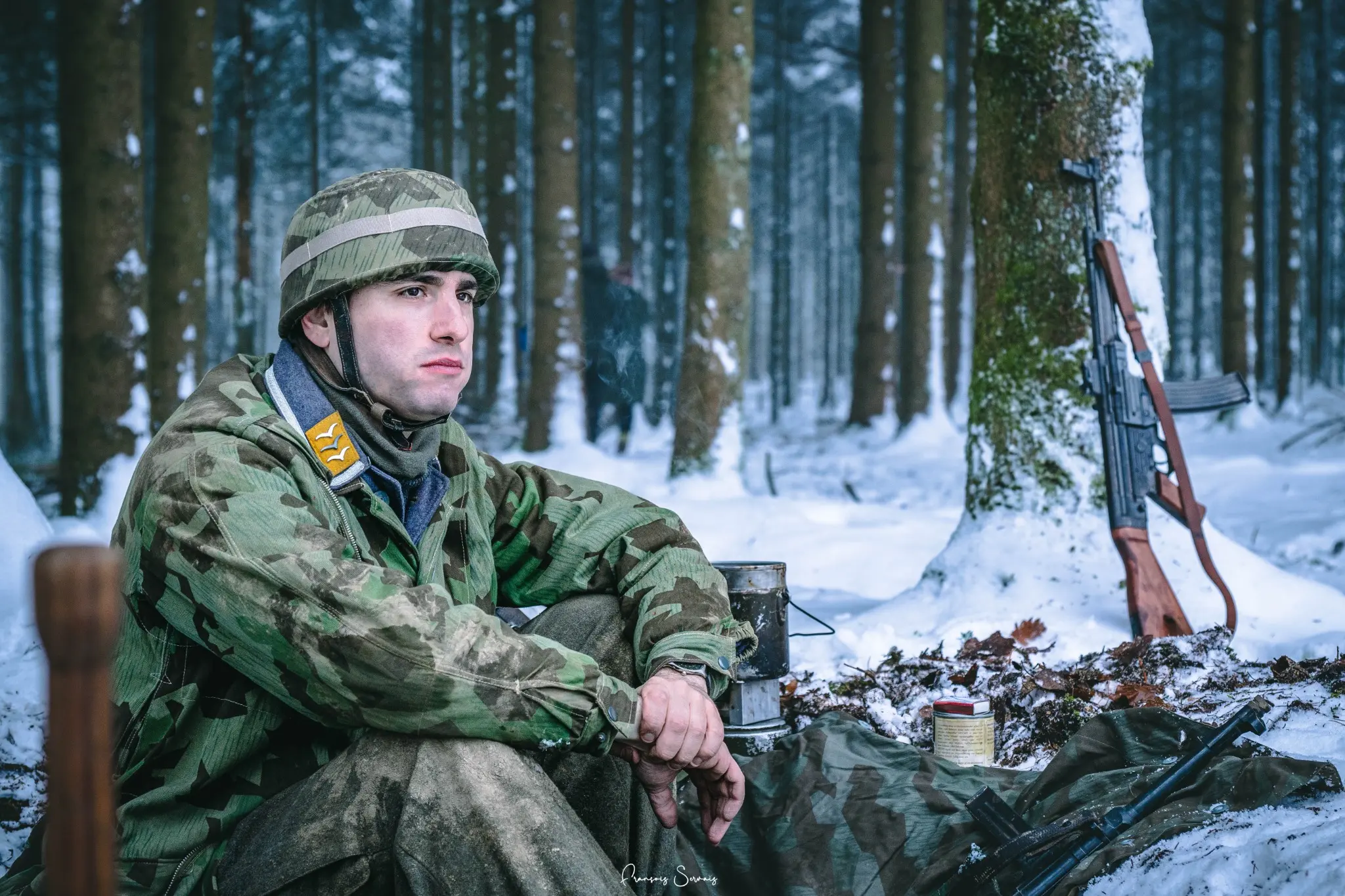 Participant en tenue militaire historique assis dans la neige au cœur de la forêt de Thirimont